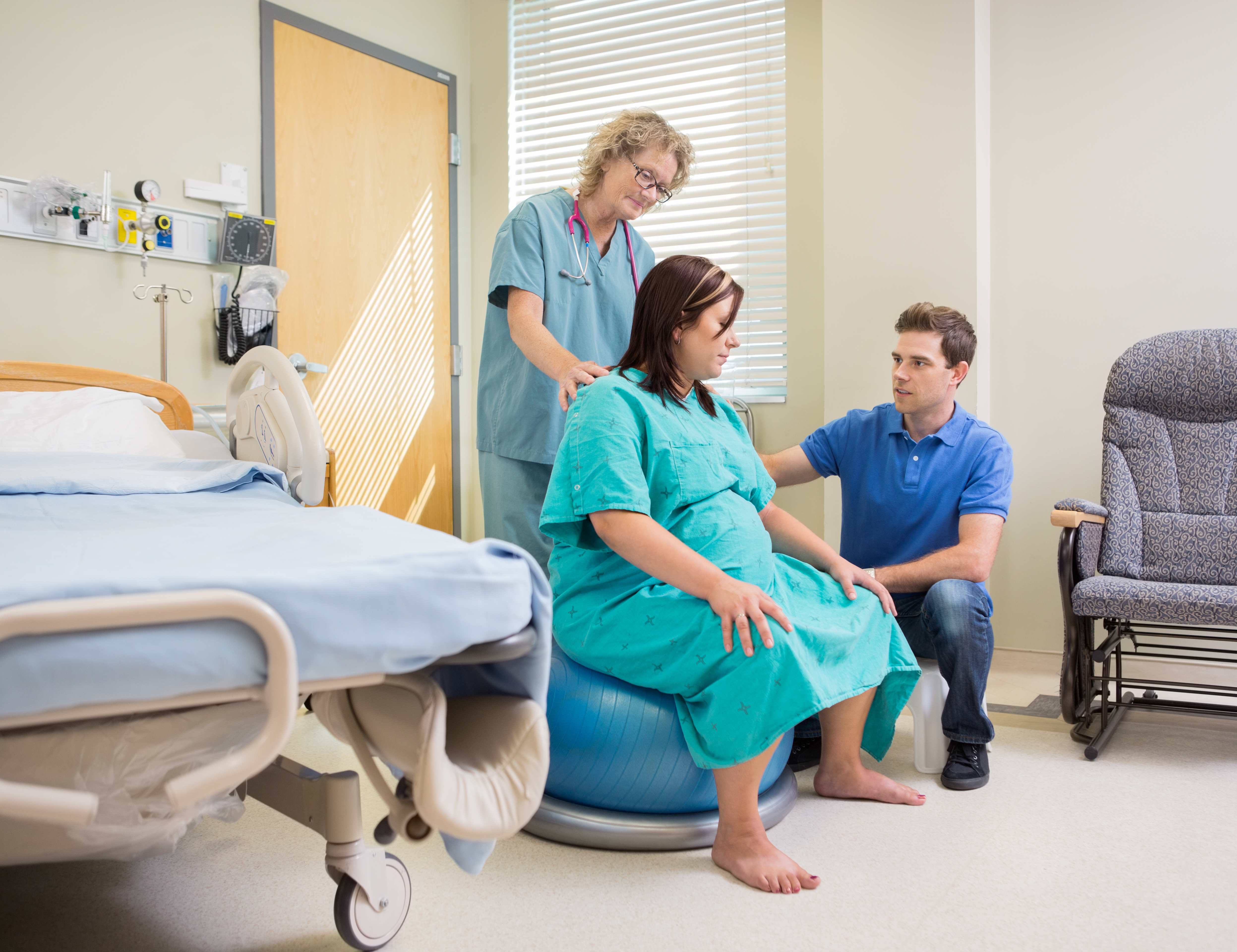 Pregnant woman sitting on Swiss ball with partner and nurse