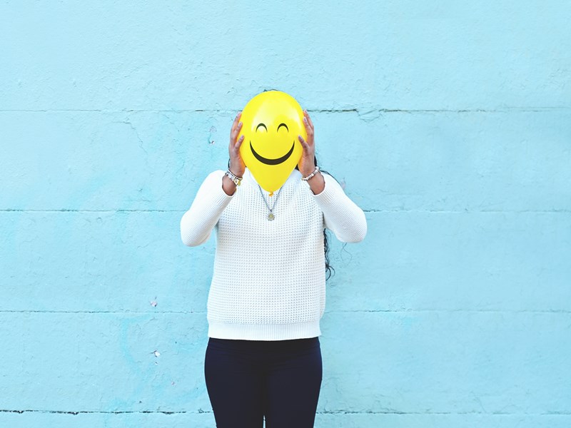 Someone holding a balloon with a happy face in front of their own face
